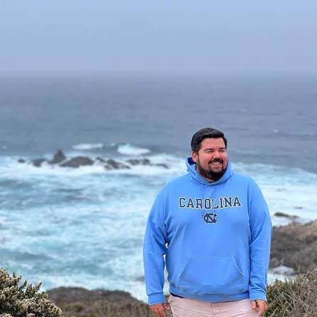 Allen Longstreet author of underbelly standing in front of the ocean in a blue sweatshirt that says "California".